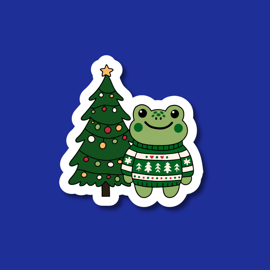 A sticker depicting a frog wearing a green sweater next to a Christmas tree.