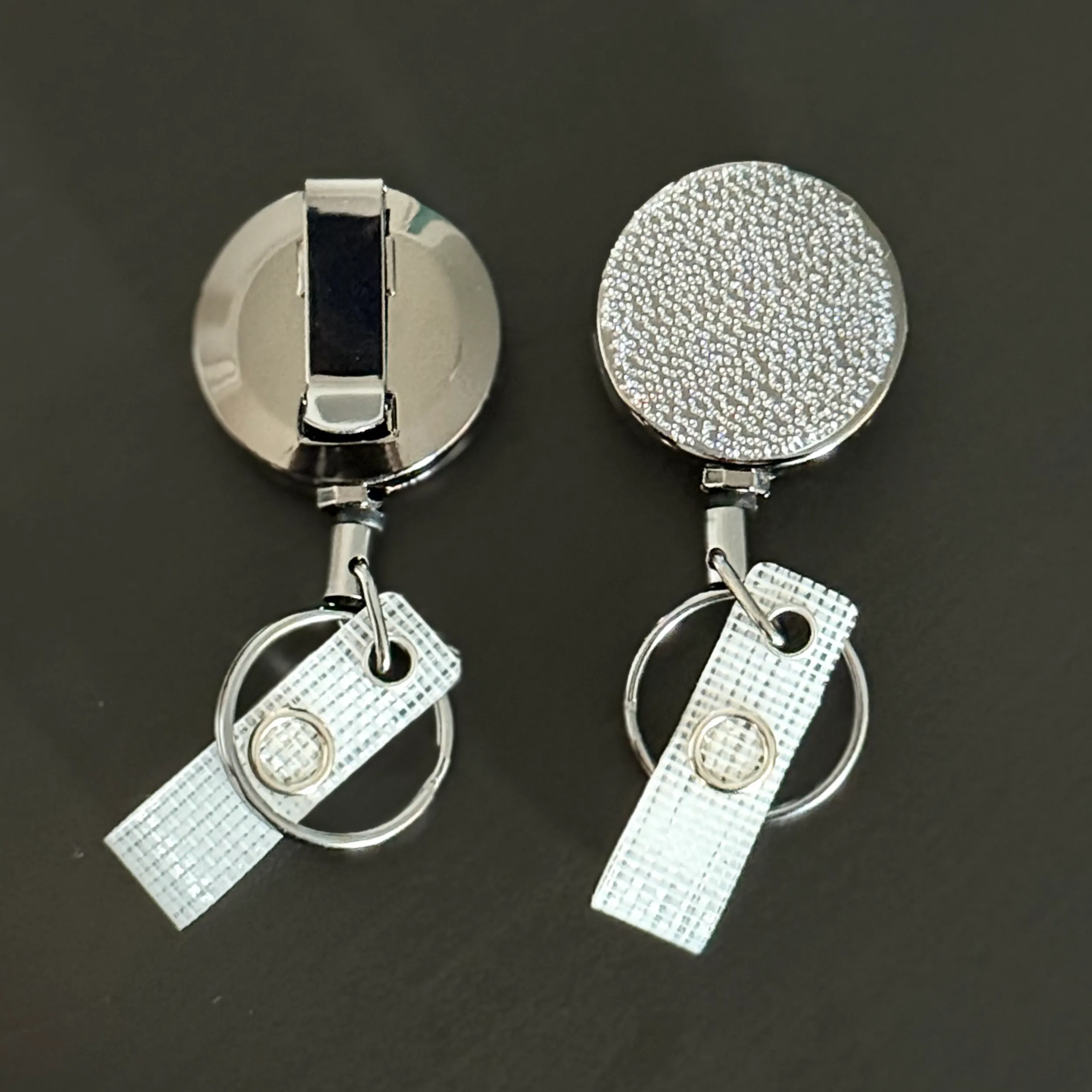 two silver-colored metal badges or keys with a textured surface, attached to a chain or ring.